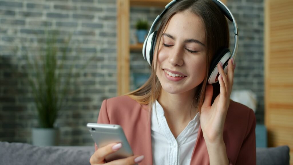 Mujer joven con auriculares escuchando un podcast en su celular, sentada en un sillón